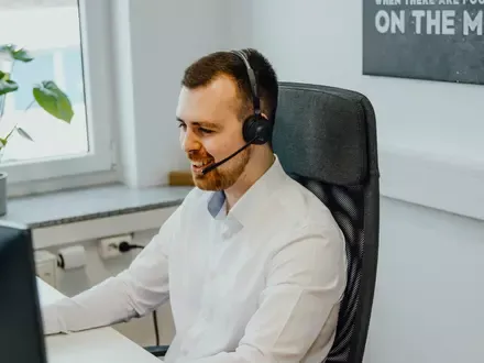 A man wearing a headset sitting in a chair behind a desk.